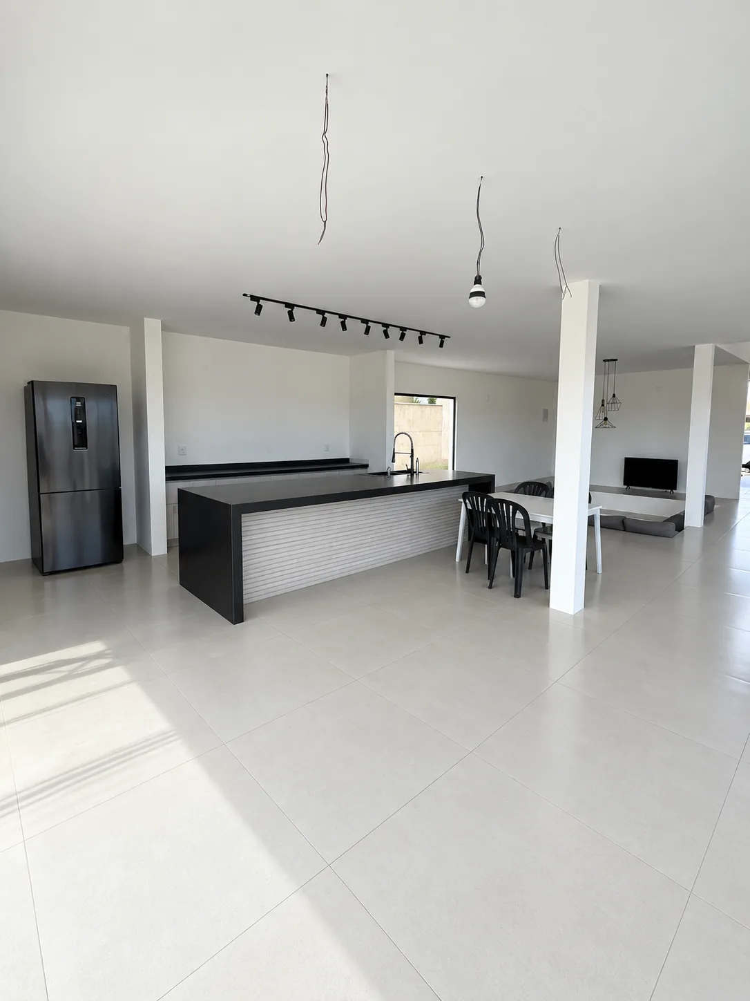 Cozinha integrada da Casa Branca, com ilha de bancada preta e sala de jantar ao fundo