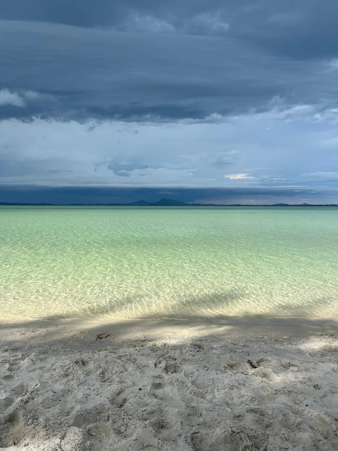 Água verde-esmeralda rasa em Arraial do Cabo, sob um céu carregado de nuvens de tempestade