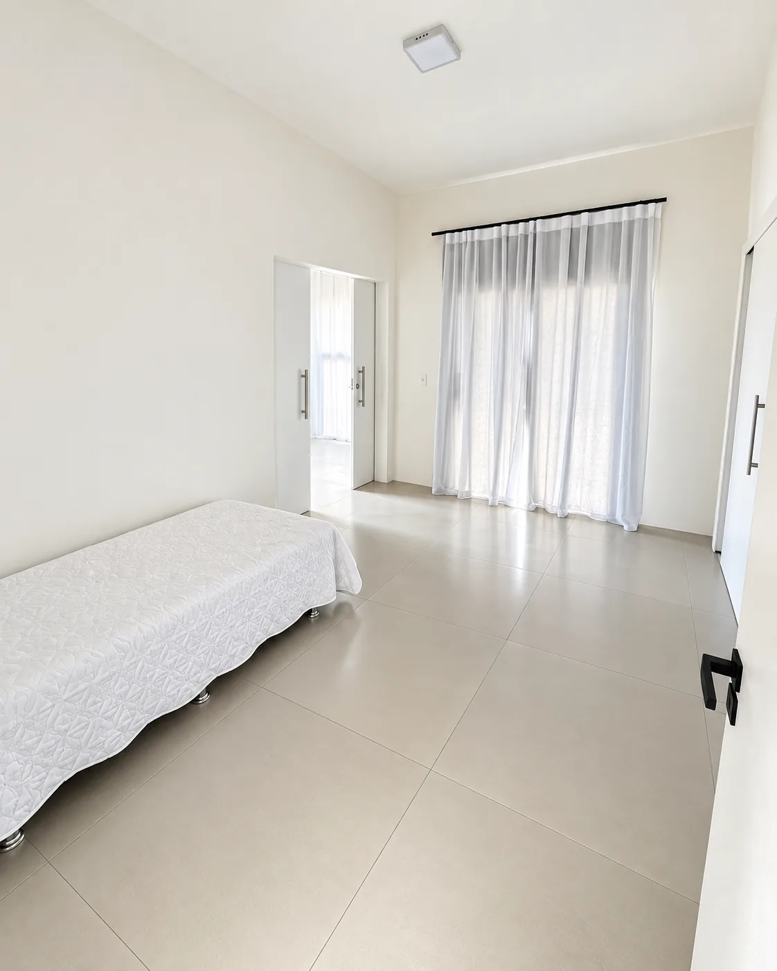 Quarto da Casa Branca com cama, cortina clara e passagem para o ambiente vizinho